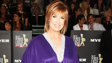 TV personality in purple dress at the Logie Awards, stands smiling with attendees visible in the background.