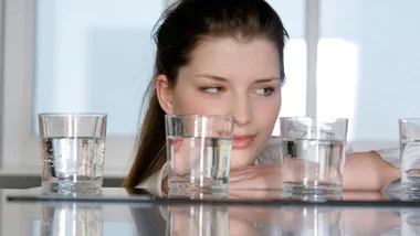Woman looking at several glasses of water on a table.