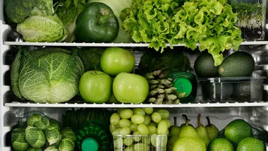 Fresh greens and fruits neatly arranged in a refrigerator, including lettuce, cabbage, apples, avocados, and pears.