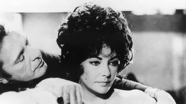 A man gently holds a woman who looks pensive, both in vintage black-and-white attire.
