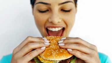 A person happily about to eat a large sesame seed burger, showing excitement and appetite.