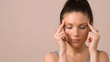 Woman with eyes closed, pressing fingers to temples, possibly experiencing a headache or migraine.