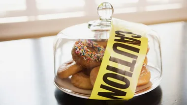 Donuts under a glass dome wrapped with yellow caution tape, suggesting dietary warning.