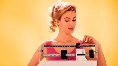 A woman in a pink tank top adjusting a mechanical scale against a yellow background.
