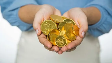 Hands holding a pile of shiny gold coins.