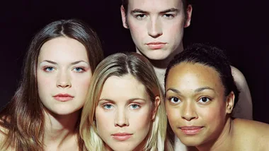 Four people with neutral expressions posed closely in front of a dark background.