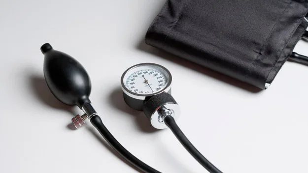 Blood pressure cuff and gauge on a white surface, used for measuring hypertension levels.