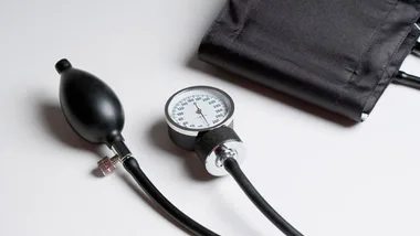 Blood pressure cuff and gauge on a white surface, used for measuring hypertension levels.