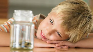 Child gazing at a jar of coins with a thoughtful expression, illustrating a concept of saving or managing pocket money.