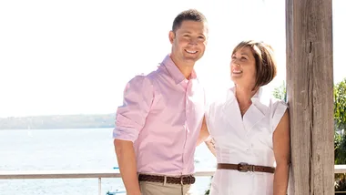 Man in pink shirt and woman in white dress smiling together by a waterfront.
