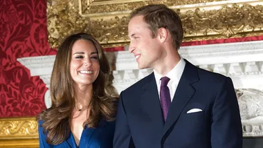 Couple standing together, smiling, in formal attire, against an ornate background.