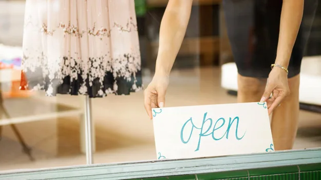 women putting an open sign in shop window, thinkstock