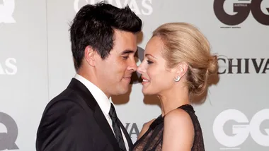 A couple embracing at a formal event, both dressed in evening wear, smiling at each other closely.