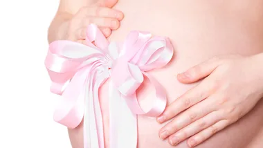 Pregnant belly with hands gently holding it, adorned with a pink and white ribbon bow.