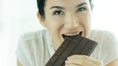 Woman eating a chocolate bar for article on stealthy superfoods.