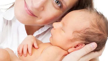 A woman lovingly holds a newborn baby close to her face, both appearing calm and content.