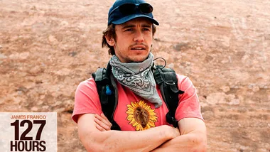Man in a cap and scarf outdoors with folded arms, promotional image from "127 Hours."