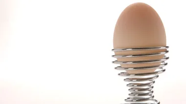 A boiled egg in a silver spiral egg cup against a white background.