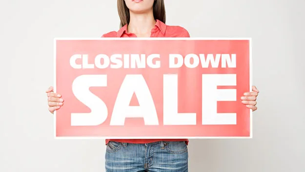 Woman holding up closing down sale sign, getty