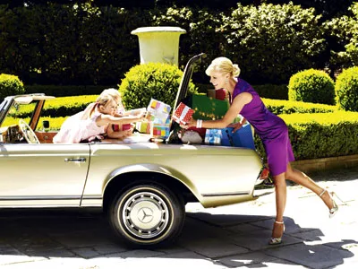Woman in purple dress puts gifts in car trunk, child inside reaches for them, set in a sunny, lush garden.