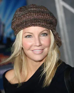 Woman smiling, wearing a brown knit hat with long blonde hair against a blurred background.