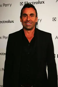 Man in a black suit smiling at the camera, standing in front of a backdrop with logos.