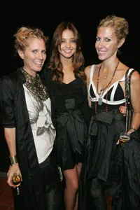 Three women smiling and posing together at an event, wearing stylish black outfits.