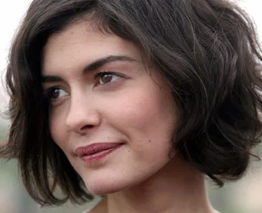 A woman with short dark hair and a soft smile looks away from the camera, surrounded by a blurred outdoor background.