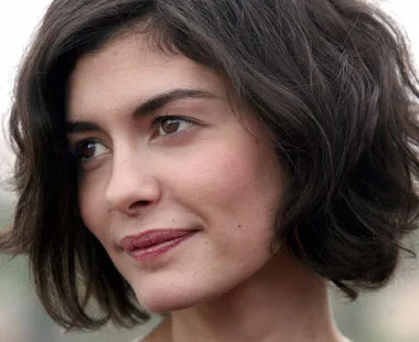 A woman with short dark hair and a soft smile looks away from the camera, surrounded by a blurred outdoor background.