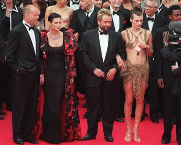 Group of four people on the red carpet at Cannes, wearing formal attire, including a woman in a distinctive beaded outfit.