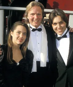Three people dressed formally, standing together at an event, smiling at the camera.