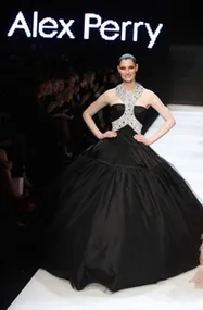 Model wearing a black gown with silver halter neck on runway; "Alex Perry" text in background.
