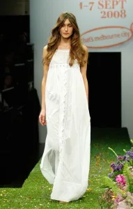 Model in a flowing white dress walks on a grassy runway at Melbourne Spring Fashion Week 2008.