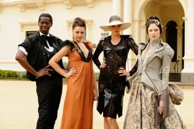 Four models in elegant outfits pose confidently in front of an ornate building at a fashion event.