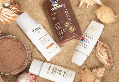 Sunscreen and tanning lotions on sand with seashells, featuring brands like Dove, L'Oréal, and Neutrogena.