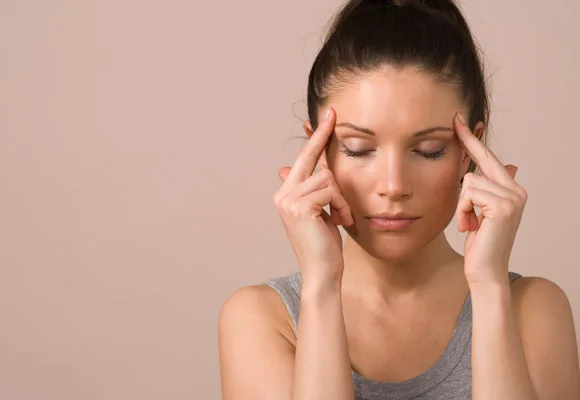 Woman with eyes closed, pressing fingers to temples, appears to have a headache.