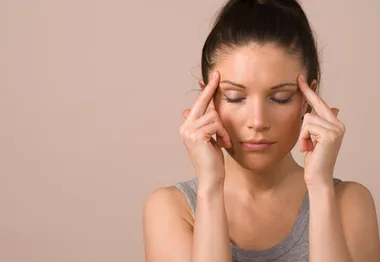 Woman with eyes closed, pressing fingers to temples, appears to have a headache.
