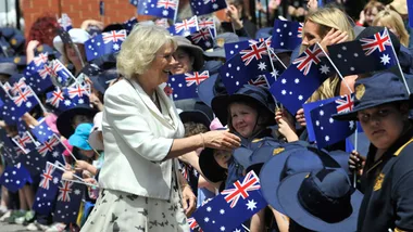 A woman greets children waving Australian flags during a public event.