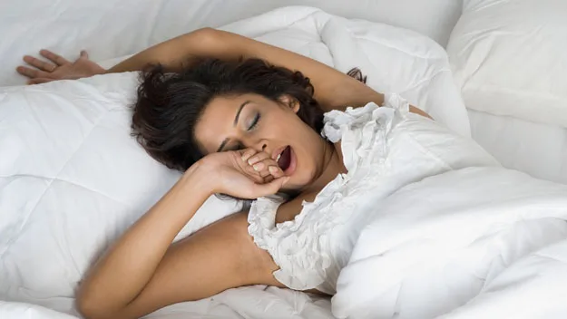 A person yawning and stretching in bed, appearing tired or waking up.