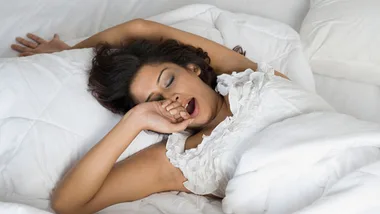 A person yawning and stretching in bed, appearing tired or waking up.