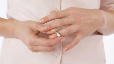 Hands of a person in a light pink shirt, fiddling with a wedding ring on their finger.