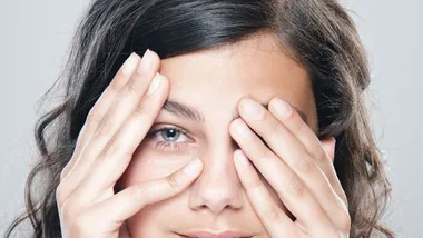 Person peeking through fingers with a playful expression, suggesting facing fears.