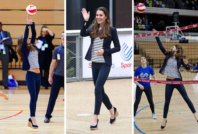 The woman plays volleyball and waves, dressed in a striped shirt and pants in a sports arena.
