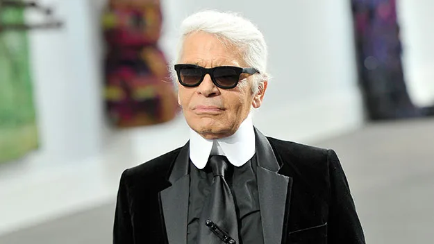 Karl Lagerfeld wearing sunglasses and a black suit with a white shirt collar.