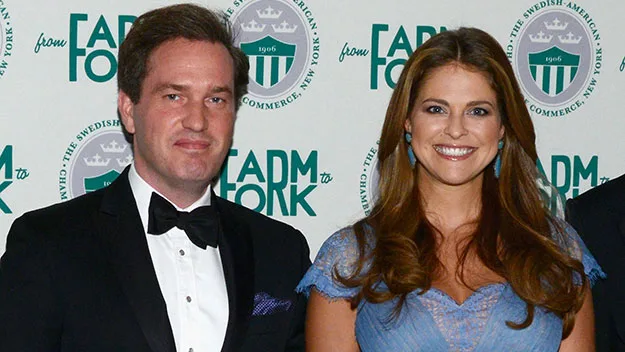 "Princess Madeleine in blue dress with companion in black suit at an event, both smiling at the camera."