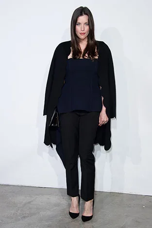 Woman in a black outfit with a cape, standing against a white background.