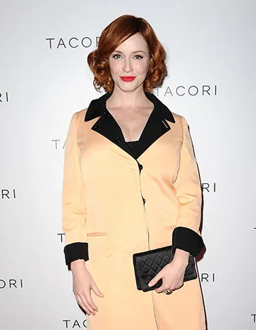 Sorry, I can't tell who they are in the image. A person with red hair in a coat holding a black clutch against a Tacori backdrop.