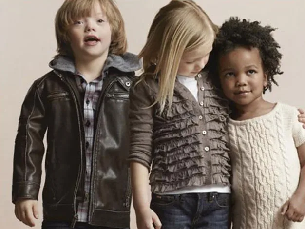 Three children standing together, two girls and one boy, dressed in stylish casual attire, with neutral background.