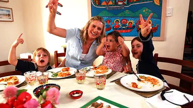 Happy family enjoying a meal with tofu and greens at a decorated dining table.