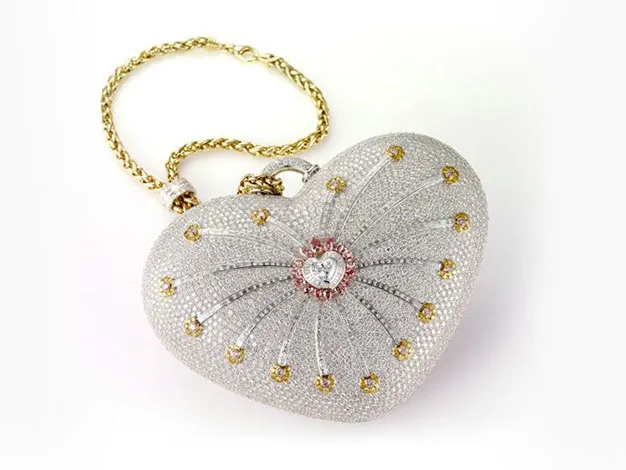 Heart-shaped diamond handbag with gold chain, featuring intricate designs and central gem accent on a white background.